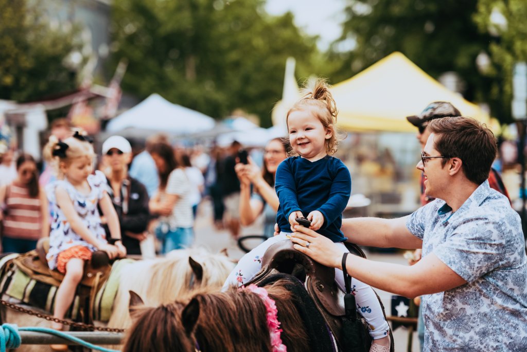 A young girl riding a horse with her parent guiding her at Franklin's Main Street Festival.